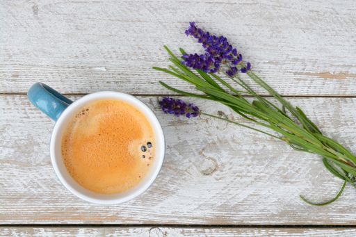 A closeup shot of a cup of coffee with lavender flowers on a wooden surface