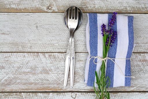 A top view of a silver fork and spoon on a wooden surface with lavender flowers laid on a towel tied with a thread