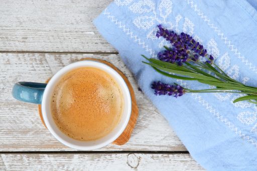 A cup of coffee and a blue kitchen towel with Lavender flower isolated on the wooden surface