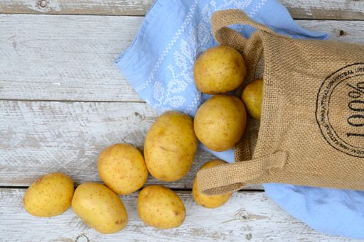 A high angle shot of the potatoes with a burlap sack and blue kitchen towel on the wooden surface