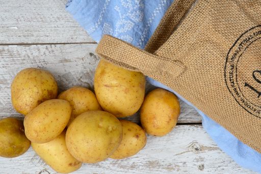 A closeup shot of potatoes with a woven bag and blue fabric cloth on a wooden surface