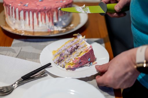 A photo of man's hands holding a piece of a birthday cake slice in a plate and a knife