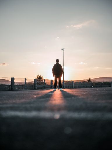 A vertical low angle shot of a back view of a male standing in the street at the sunset