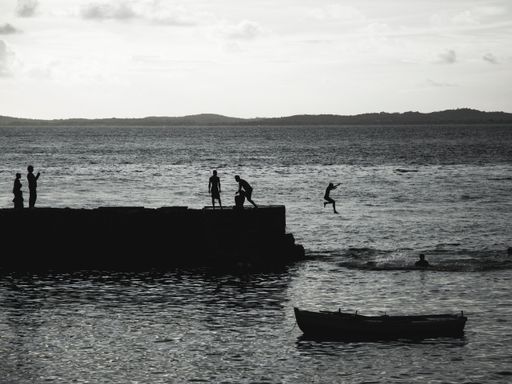 A grayscale shot of a young group of people jumping from the pier of Porto da Barra in Bahia, Brazil.