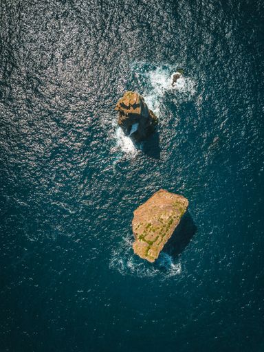 The aerial view of the rocks in a sea on a sunny day
