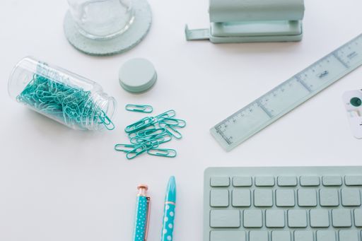 A closeup of a turquoise computer keyboard next to paperclips and other stationery items of the same color
