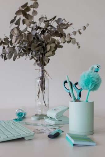 A turquoise computer keyboard, pens, paperclips, scissors, and other stationery items next to flower branches