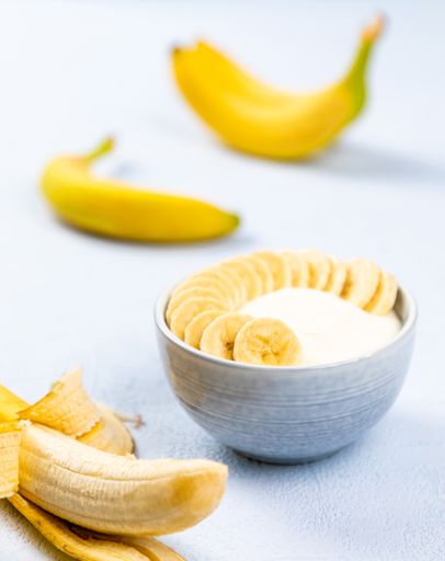 A closeup shot of cream dessert with banana fruit in a bowl on light blue background