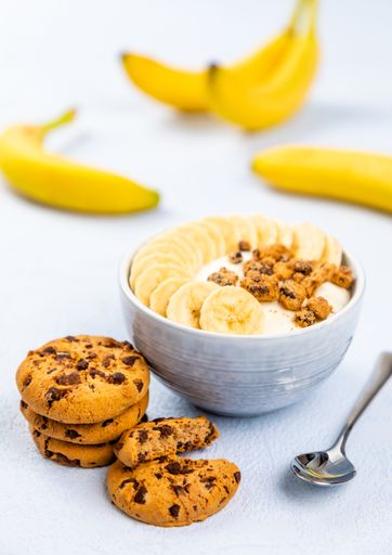 A closeup shot of cream dessert with banana fruit in a bowl and cockies on blue background