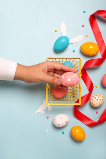 A top view shot of a hand holding eggs on a basket on a blue table with colorful easter eggs