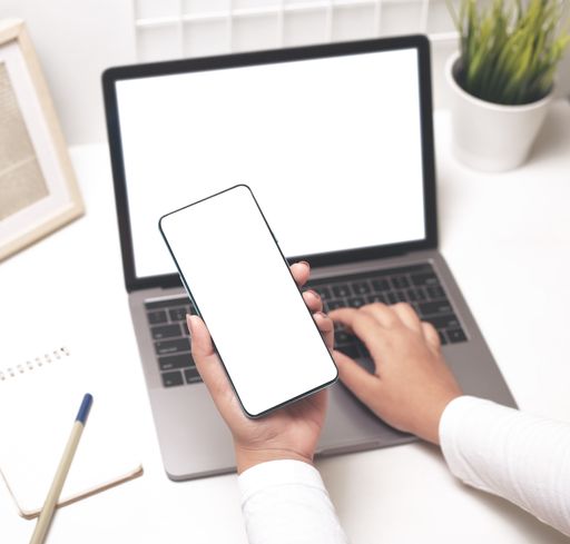 A closeup shot of female hands using a laptop and mobile phone with a blank screen on the office