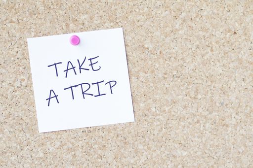 The words "take a trip" on a paper attached to a board with a pin