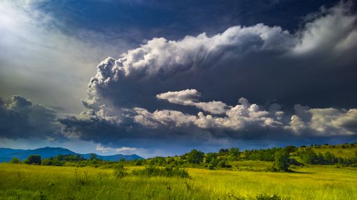 A horizontal shot dramatic puffy clouds over a green field