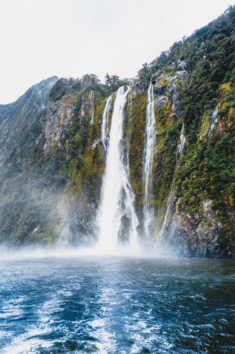 A gorgeous vertical shot of a waterfall over a fresh pond surrounded by lush greenery in the Milford Sounds in New Zealand