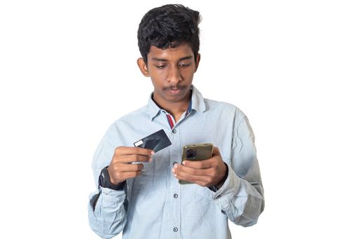 A South Asian male paying online using a smartphone and a credit card isolated with white background