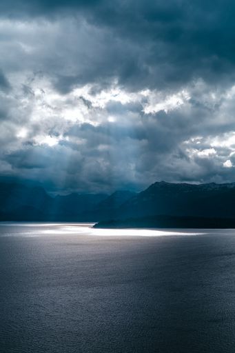 A vertical shot of a beautiful view of the lake, mountains, and the sunbeams through the clouds