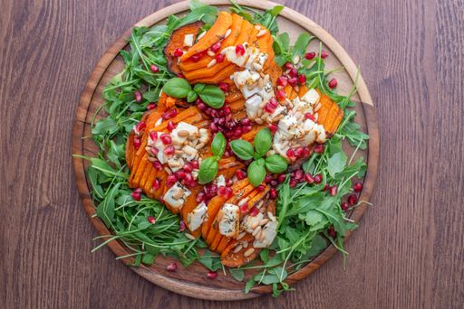 A top view of healthy salad with baked pumpkin, feta cheese, and arugula greens on a wooden plate