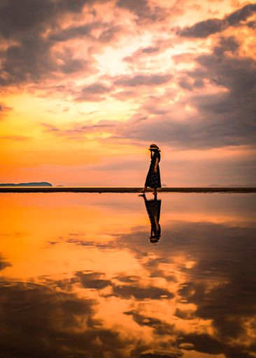 A silhouette of female walking on water with reflection during sunset