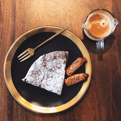 A top view of a piece of cake and two biscuits on the black and golden plate with a cup of coffee