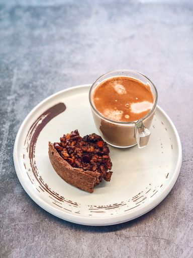 A vertical closeup of a cup of coffee with milk and a bitten slice of a pecan pie on the white plate