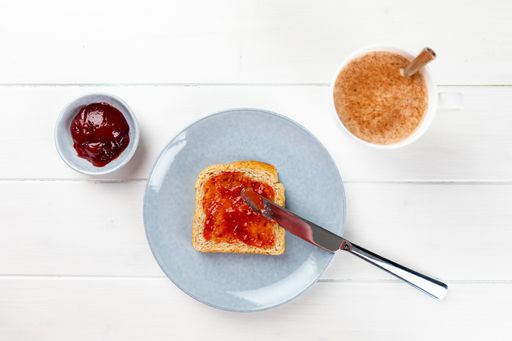 A top view of a toast with strawberry jam on a blue plate on a white wooden background