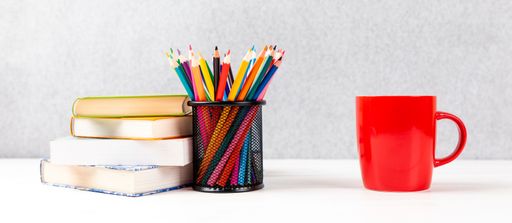 A closeup of colorful pencils, books, and red cup on a desk with a gray background and copy space