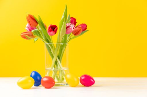 A closeup of colorful tulips in a vase with colored easter eggs and copy space