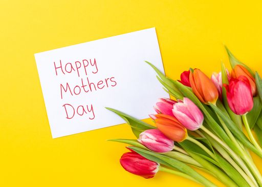 A closeup of colorful tulips on a yellow background with white paper and text happy mothers day
