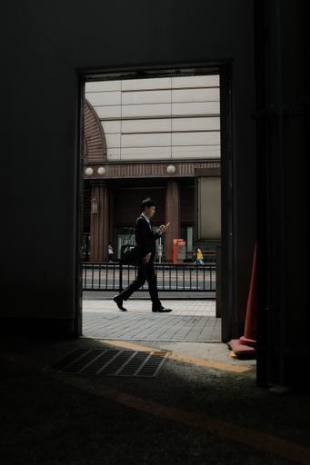 A vertical shot of a male wearing black suit walking on a sidewalk looking at his phone