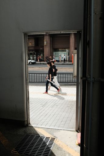 A vertical shot of a male and a female wearing black shirts walking on a pavement by the street