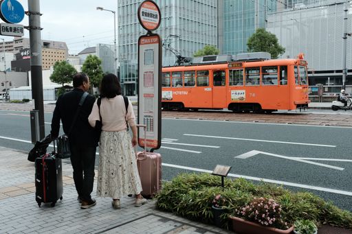 A couple with suitcases standing on a sidewalk by the street with an orange street running train