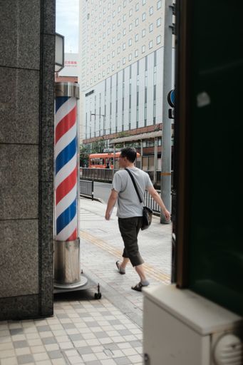 A vertical shot of a person walking near barber's pole on a sidewalk
