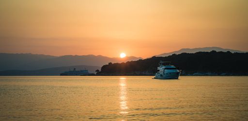 A scenic view of boats sailing against the hills covered with greenery at the sunset