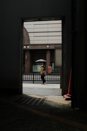 A vertical shot of a female holding an umbrella walking on a sidewalk