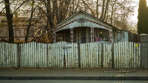 An old wooden house with a white fence along the road
