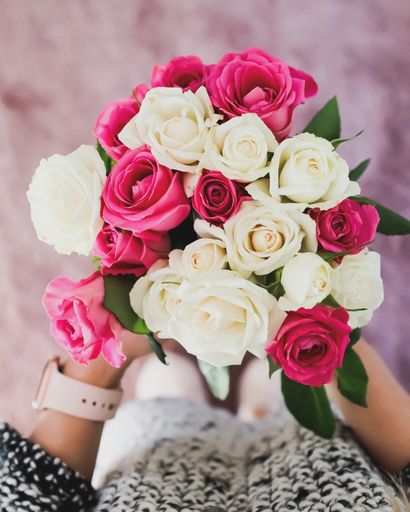 A vertical selective focus shot of a woman holding a bright pink and white rose bouquet