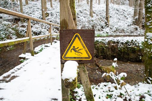 Slippery warning sign in the forest, wooden bridge covered with snow, winter season, beware of danger, outdoors