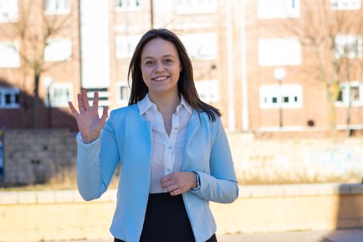 A formal dress happy businesswoman is waving her hand outdoors, look at the camera, smiling.