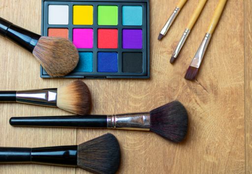 A high angle shot of an eyeshadow palette with vibrant colors and brushes on a wooden surface