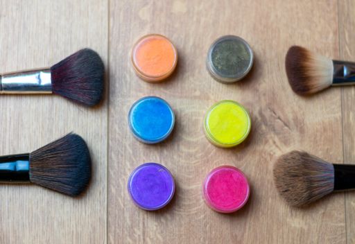 A high angle shot of colorful makeup glosses and brushes on a wooden surface