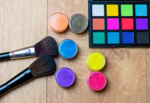 A high angle shot of eyeshadow palette, brushes, and colorful glosses on a wooden surface