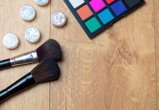 A high angle shot of eyeshadow palette, brushes, and silver glosses on a wooden surface