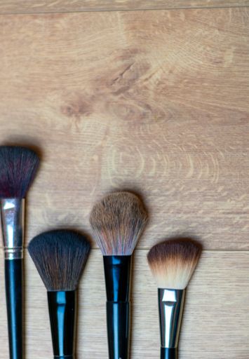 A vertical high angle shot of makeup brushes on a wooden surface