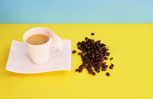 A closeup shot of a cup of coffee and coffee beans on yellow and green background