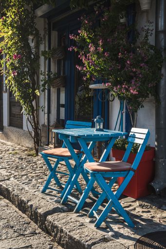 A vertical view of blue wooden chairs and a table of an outdoor cafe on a street
