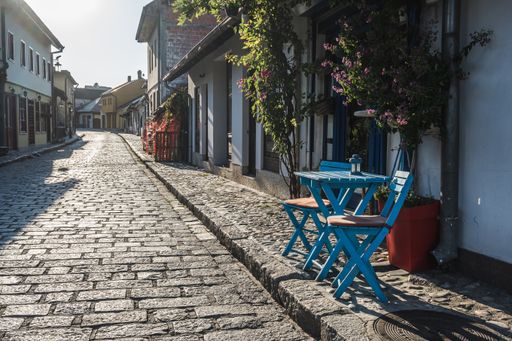 A beautiful view of blue wooden chairs and a table of an outdoor cafe on a cobblestone street