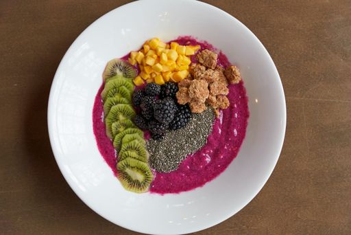A top view of an acai bowl topped with fruits and granola, in a white plate