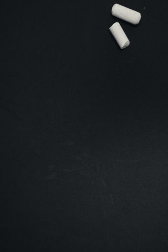 A top view of two pieces of white chalk on a blank black surface