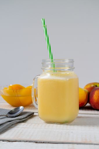 A vertical closeup shot of a mason jar of fresh natural peach juice or nectar with a tube on a table