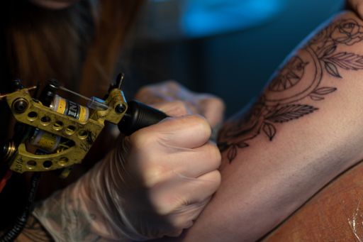 A Caucasian female tattoo artist working on a person's arm